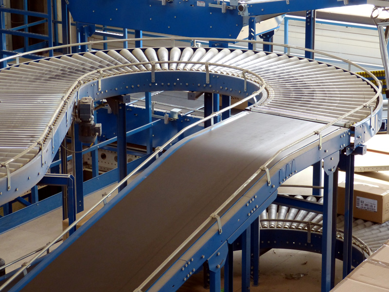Kurvenband und Rollenbahn eines Fördersystems in einer Industriehalle.